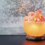 Turned on Himalayan pink salt lamp carved as a bowl on a black table.