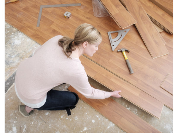 A woman working in her home on a do-it-yourself project installing laminate wood flooring. She is placing the board, as seen from above.