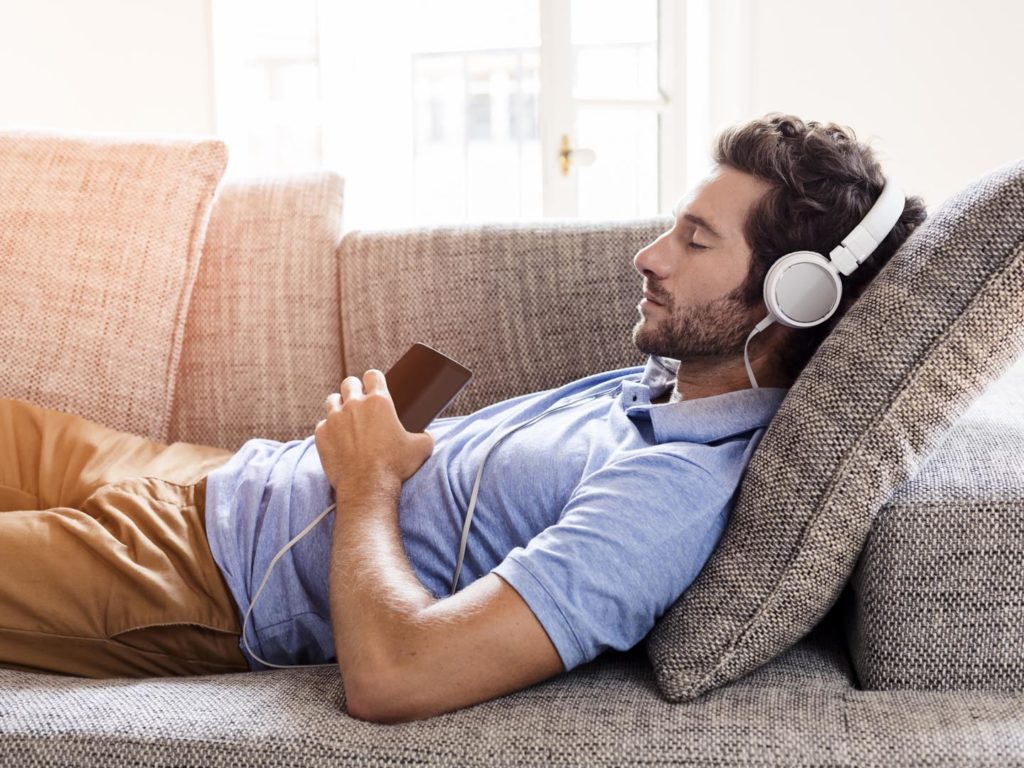 Young male couch listen headphones mobile phone at home