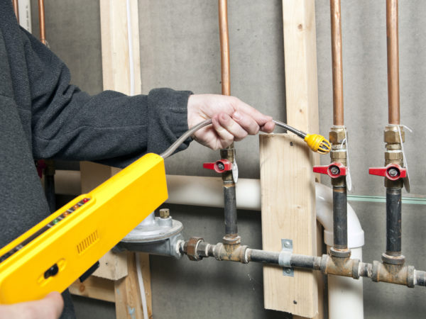 A worker is using a leak detector near a set of house gas lines at a renovation site. Very small gas leaks are often found at pipe joints in older construction.