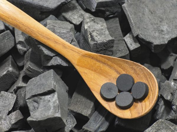 activated carbon pill in wood spoon on charcoal texture background