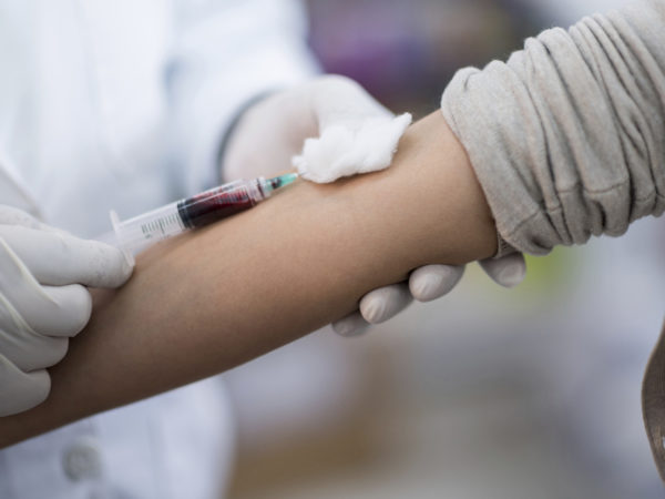 Woman donating blood and doctor holding the needle while it fills