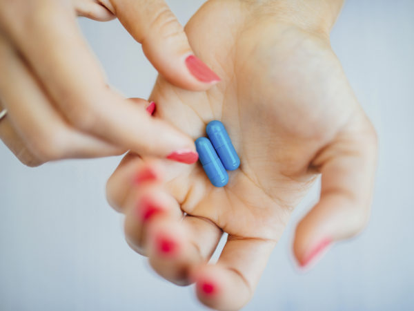 Women&#039;s fingers with pink manicure taking blue pills from hands