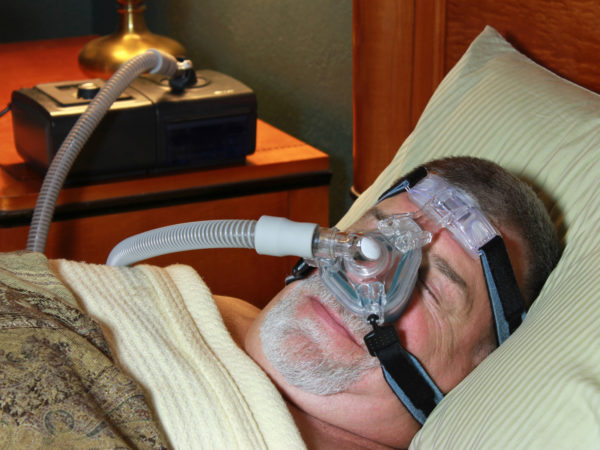 A senior man peacefully sleeps with a CPAP mask on his face.