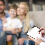 Young happy family of three talking with psychologist. Focus on psychologist. There are many books in psychologist office