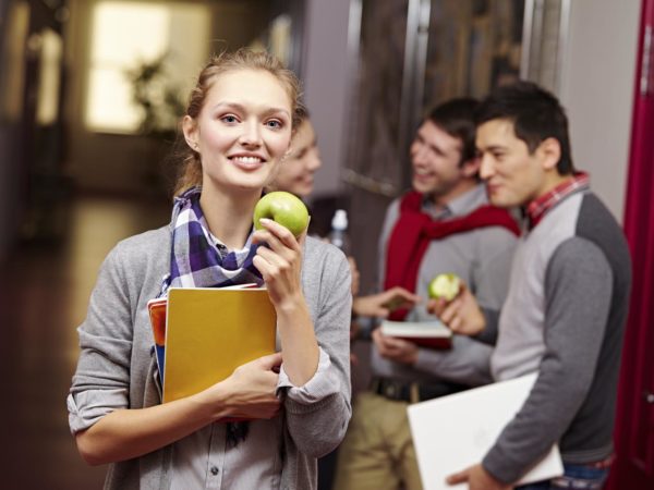 female student standing in the corridor and eating apple