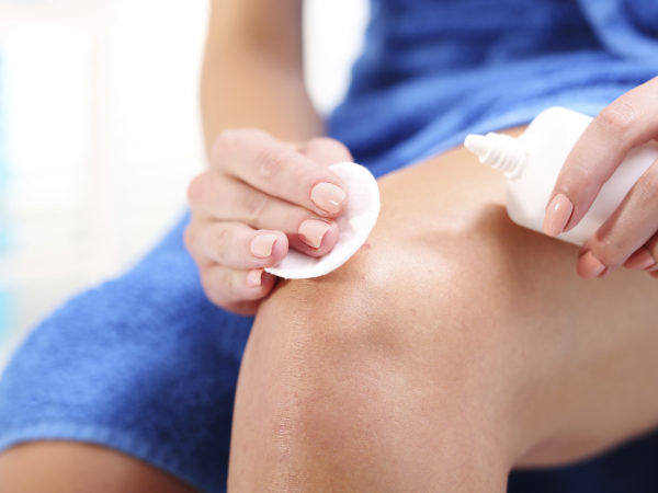 Female disinfects the wound on his knee pouring with oxygenated water.