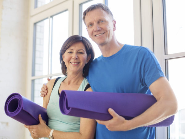 Portrait of a happy mature couple standing together holding their yoga mats at gym