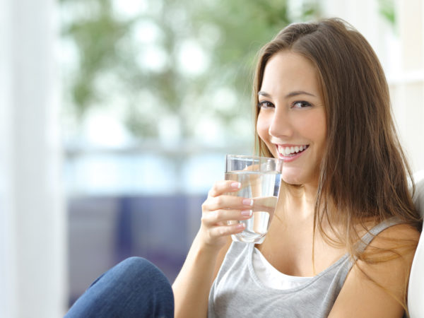 Girl drinking water sitting on a couch at home and looking at camera