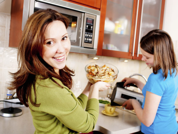 Mother and Daughter cooking, mother putting meal into microwave, girl making tea