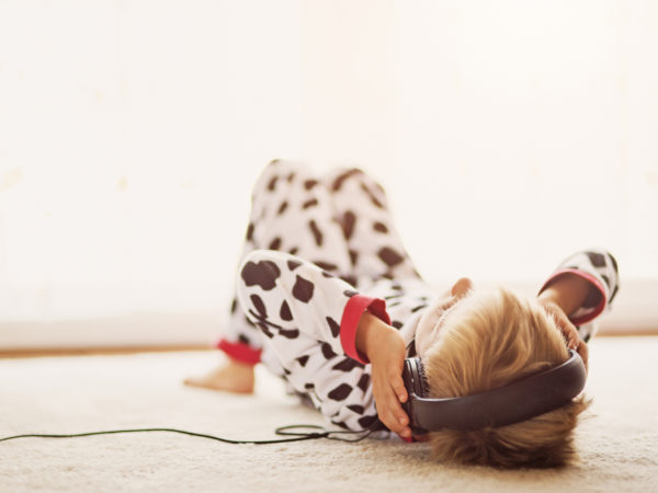 Little boy lying in pyjamas on his back near the window listening to the music in headphones.