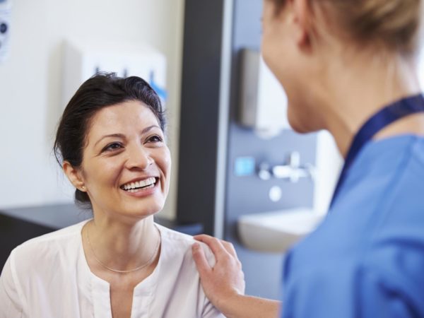 Female Patient Being Reassured By Doctor In Hospital Room