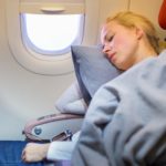 Tired blonde casual caucasian lady napping on uncomfortable seat while traveling by airplane. Commercial transportation by planes.