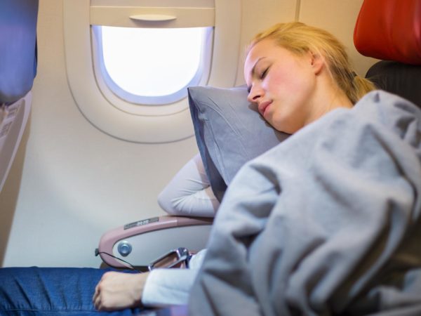 Tired blonde casual caucasian lady napping on uncomfortable seat while traveling by airplane. Commercial transportation by planes.