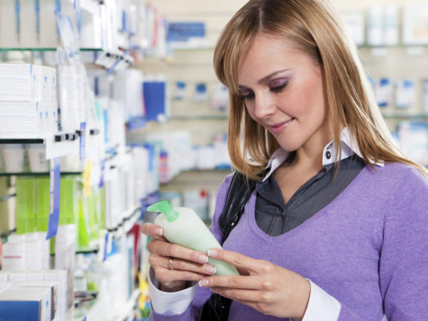 Portrait of blonde woman reading label of shampoo in pharmacy. Copy space