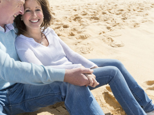 Happy mature couple sitting on the beach holding hands