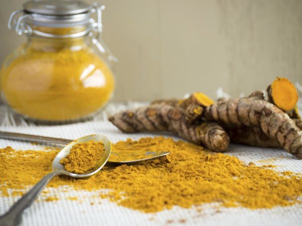 Healthy living begins with healthy food. Turmeric root may help with anti-aging. Add to food, use as a tonic, or display a healthy lifestyle. Light colored background, classic spice jar, and ground curcumin and turmeric root displayed with spoons