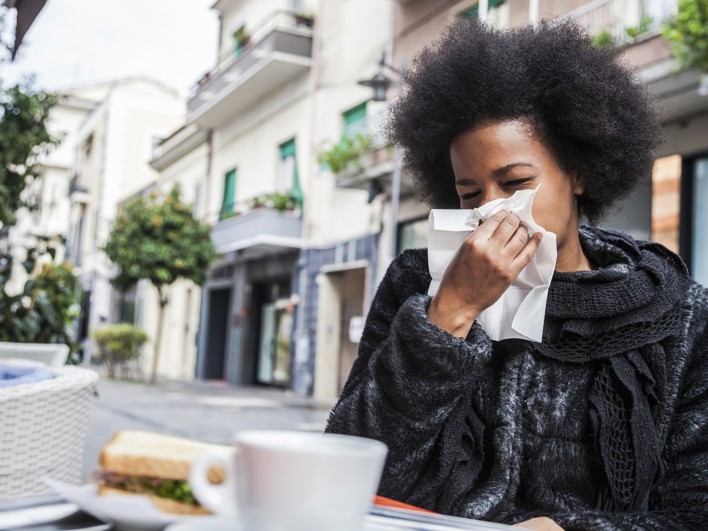 Woman sneezing due to flu during a break in a cafe using an handkerchief