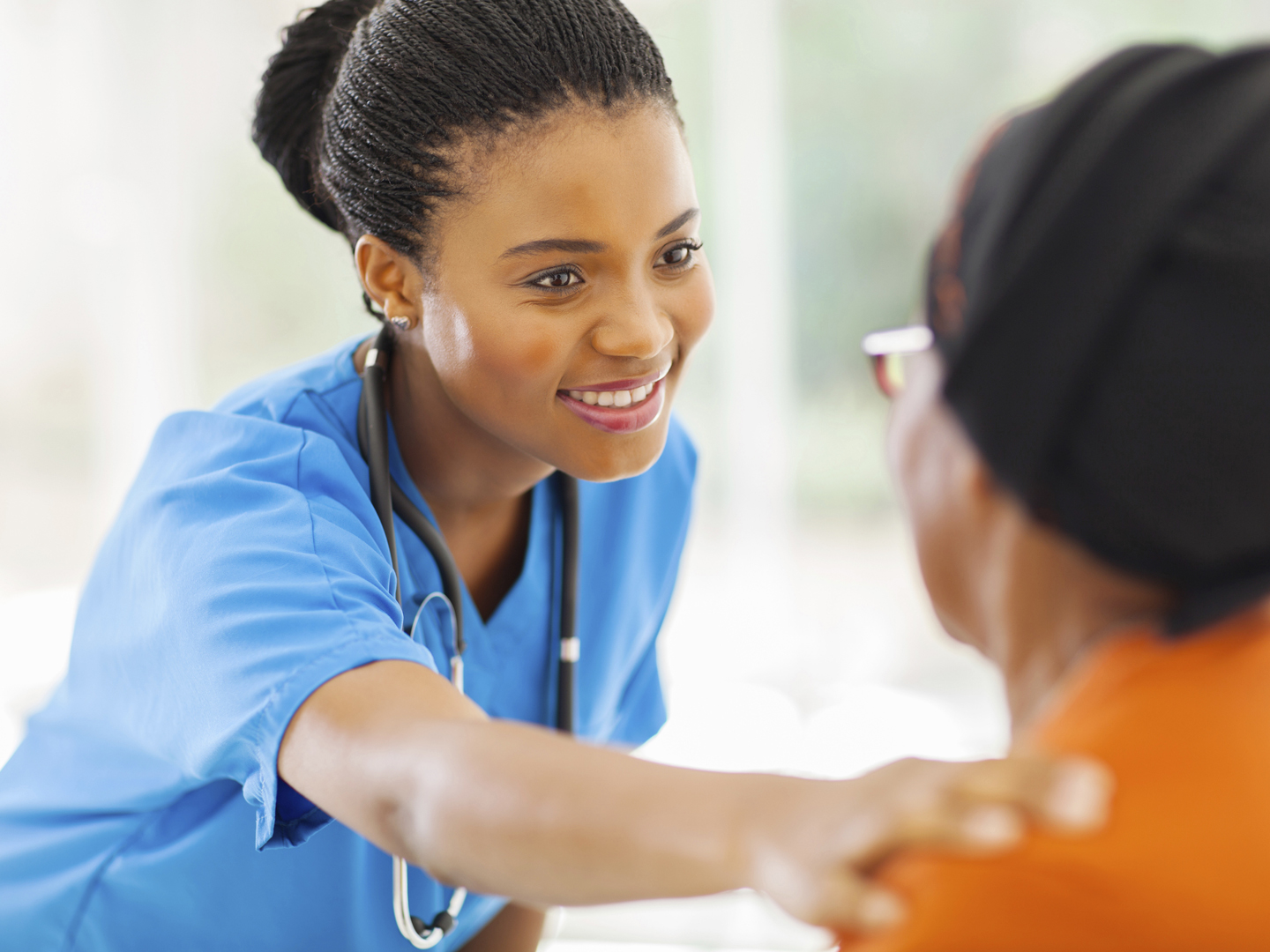 caring african medical nurse comforting senior patient in office