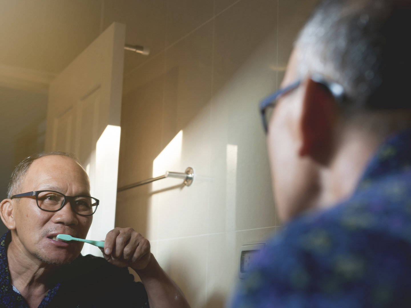 Asian oldman is Brushing Teeth and looking through the mirror in the bathroom.