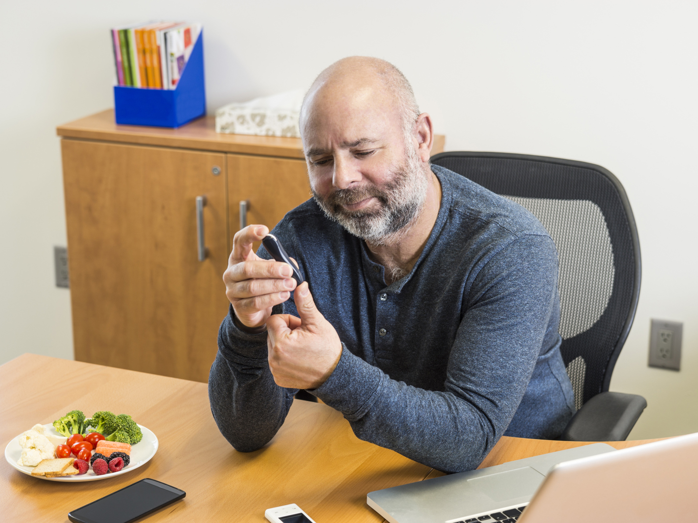 A diabetic man at work testing his blood to monitor his blood glucose levels so he can manage his diabetes.