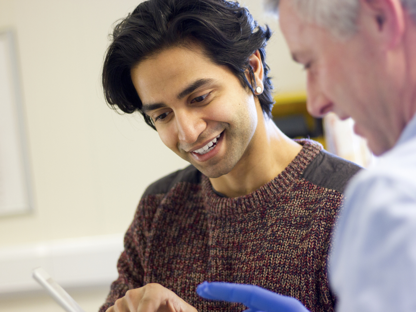 A male doctor  beside another male. They are in an examination room talking as he holds a digital tablet in one hand.  The patient looks happy as he is shown his results by the doctor. very close crop of their head and shoulders.