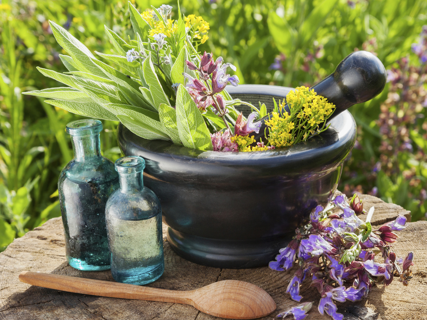 mortar with healing herbs and sage, glass bottle of essential oil outdoors