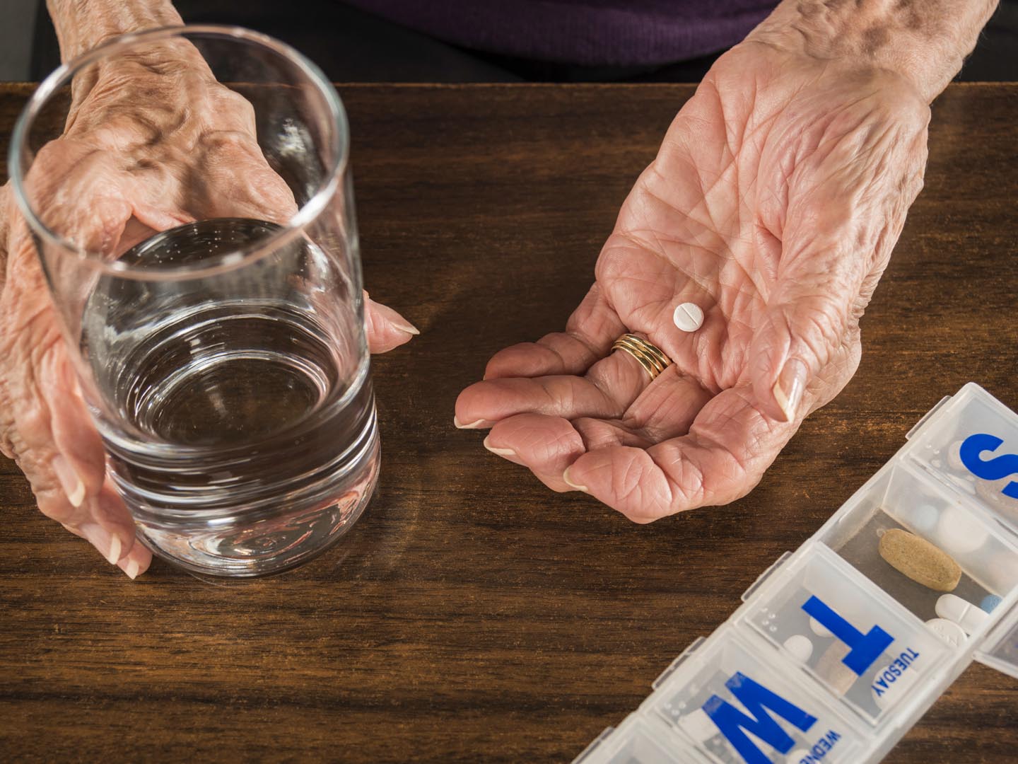 senior arthritis hands with pill organizer and glass of water