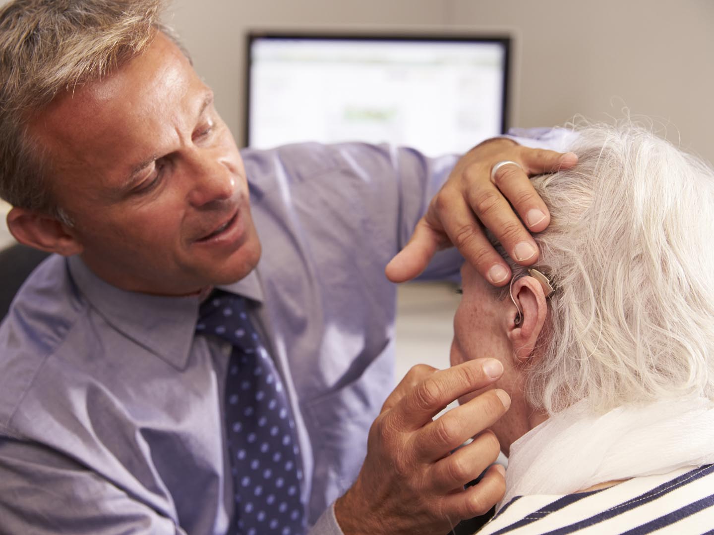 Doctor Fitting Senior Female Patient With Hearing Aid