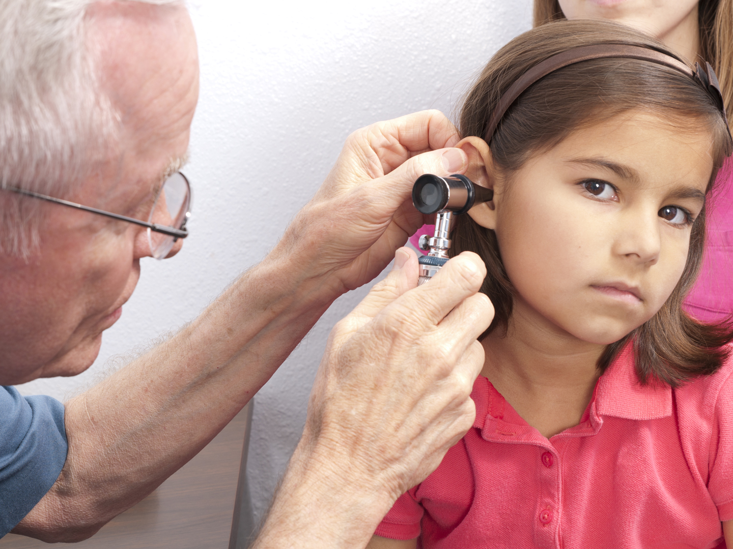 &quot;Stoic, brave young girl allows doctor to look into her ear with otoscope as she sits on her mother&#039;s lap.  He could be checking for otitis media, middle ear infection&quot;