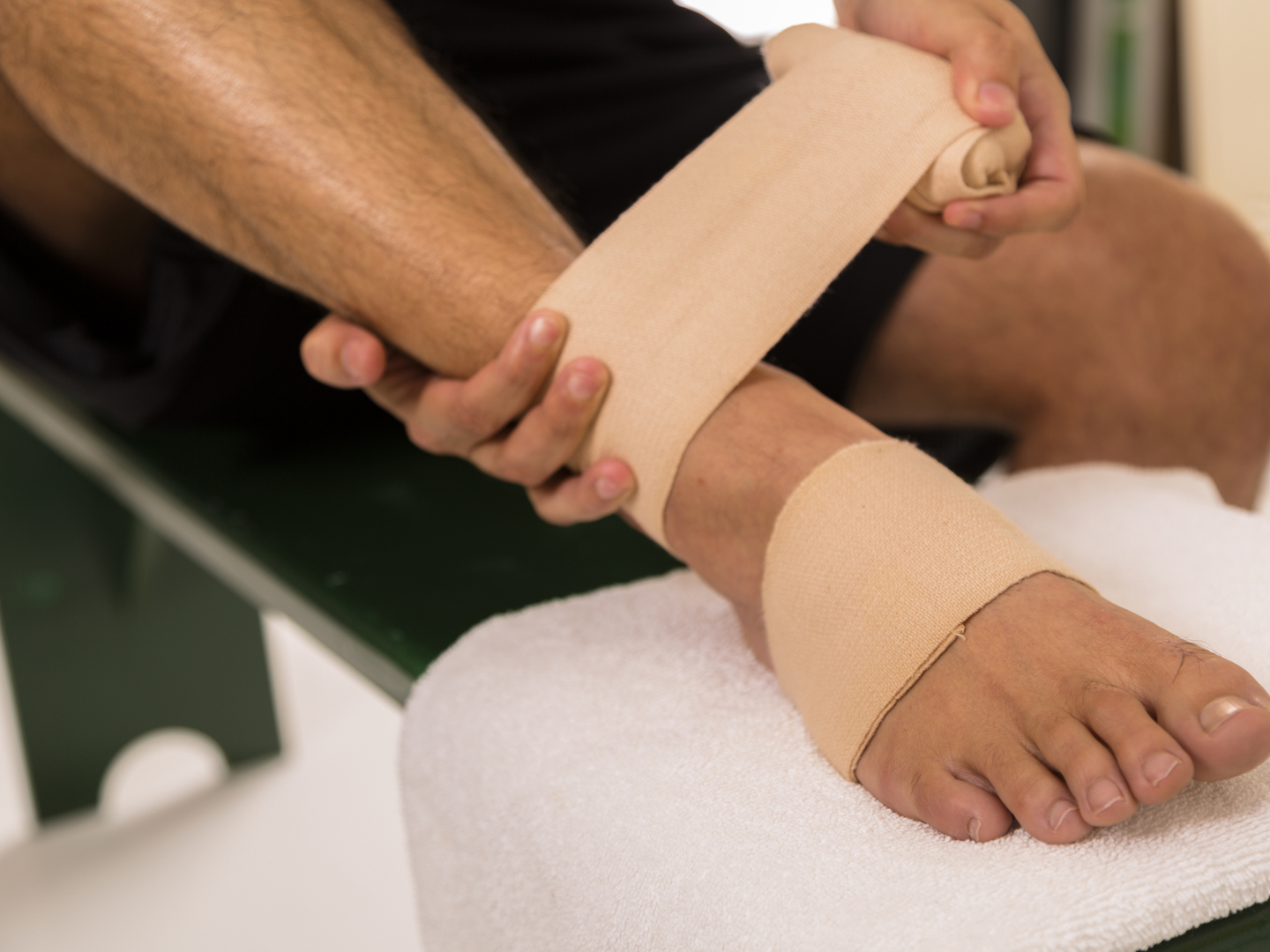 Man in sports locker room wrapping his painful ankle.