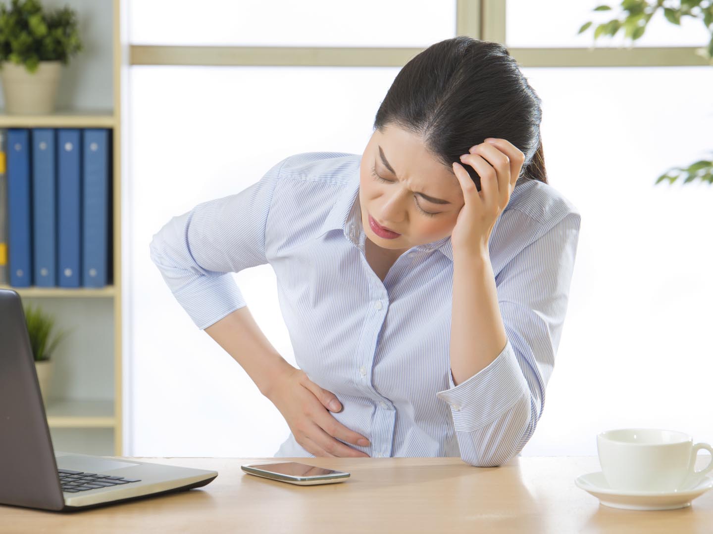 Young asian business woman with stomachache in office