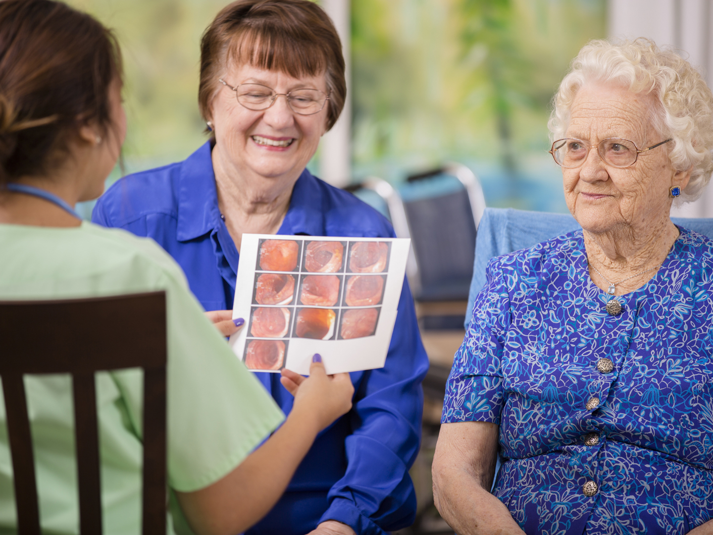Latin, female doctor or nurse conducts family consultation with elderly patient and her daughter in a nursing home or clinic setting. They discuss recent colonoscopy results. Woman is over 100 years old!