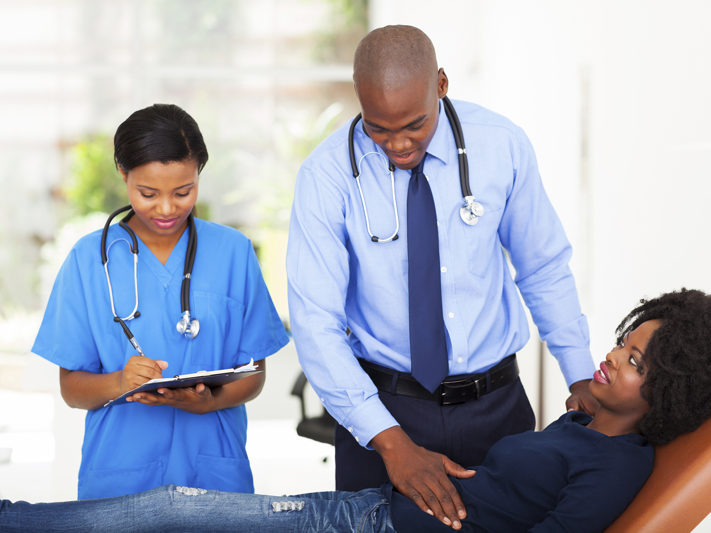 african doctor and nurse examining female patient in office