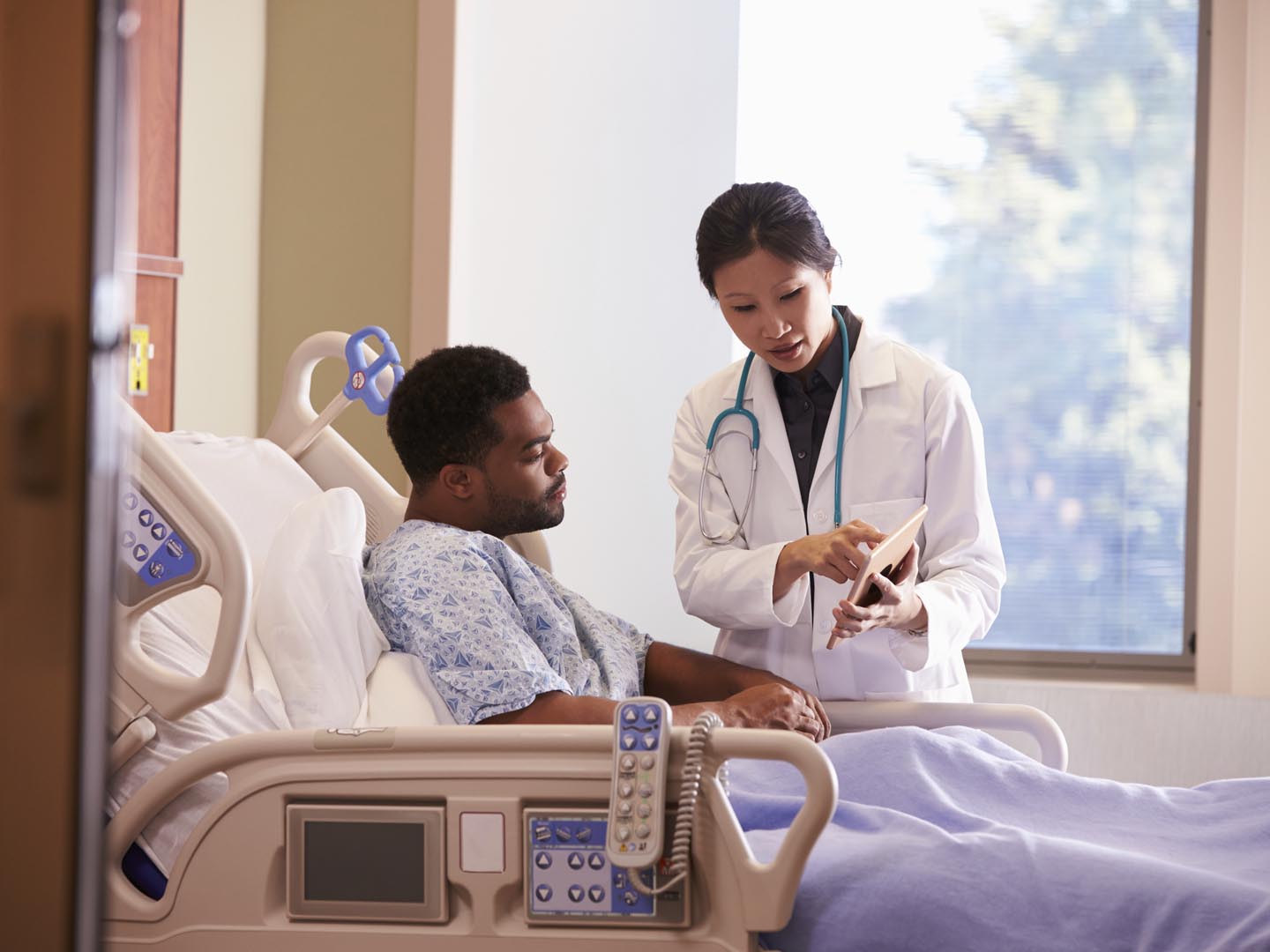 Hospital Doctor With Digital Tablet Talks To Male Patient