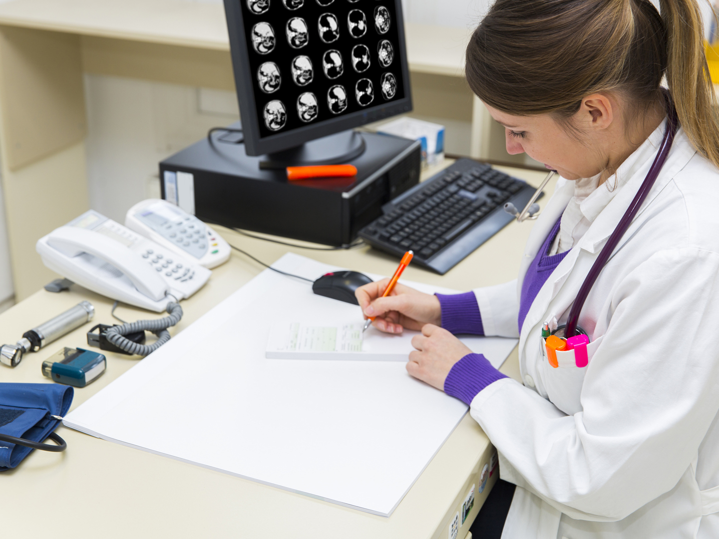 Pretty young woman doctor working,writing prescription for sick patient...CAT scan of human abdomen on monitor