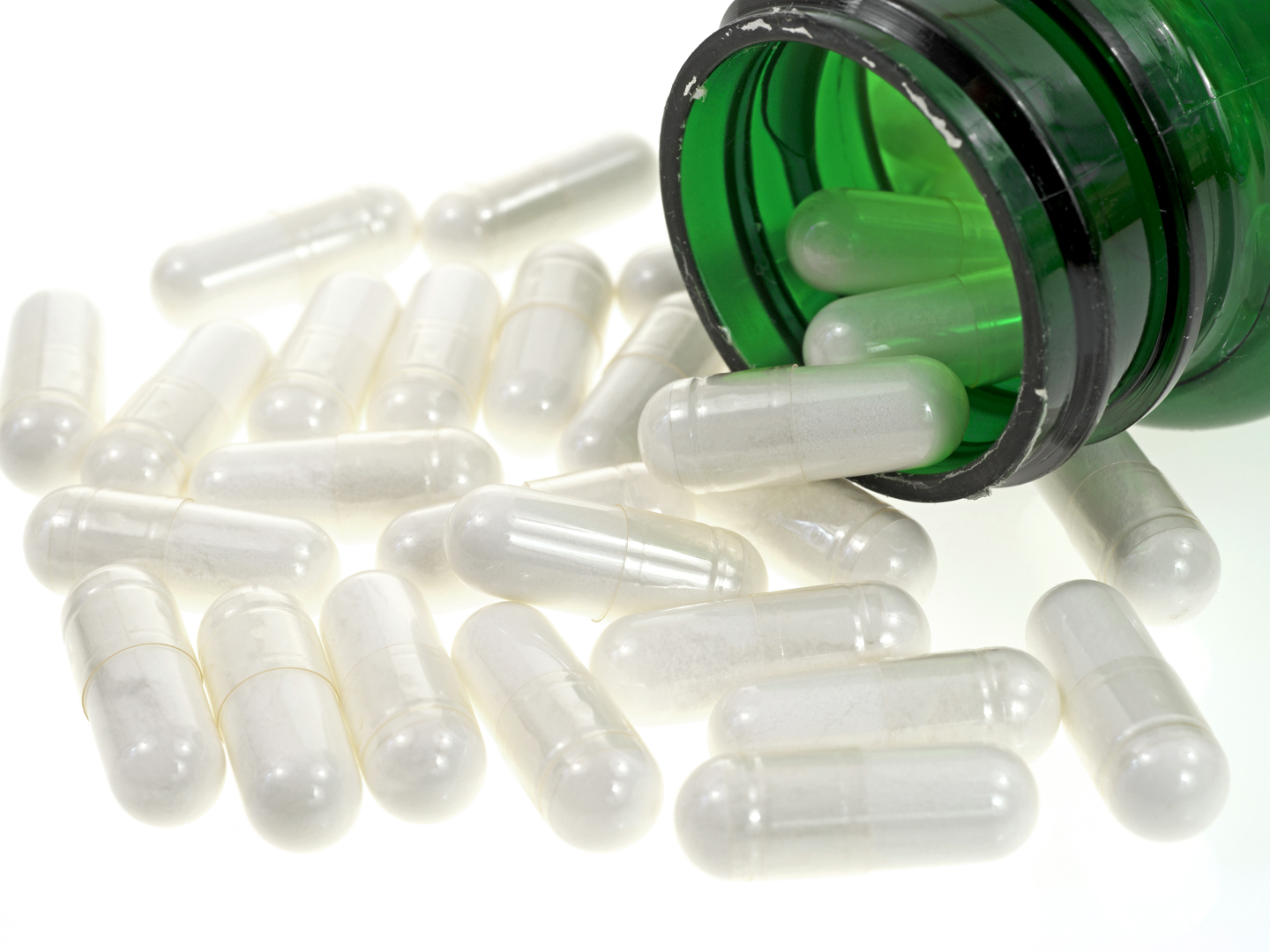 A close view of several acidophilus capsules spilling from a green vitamin bottle.