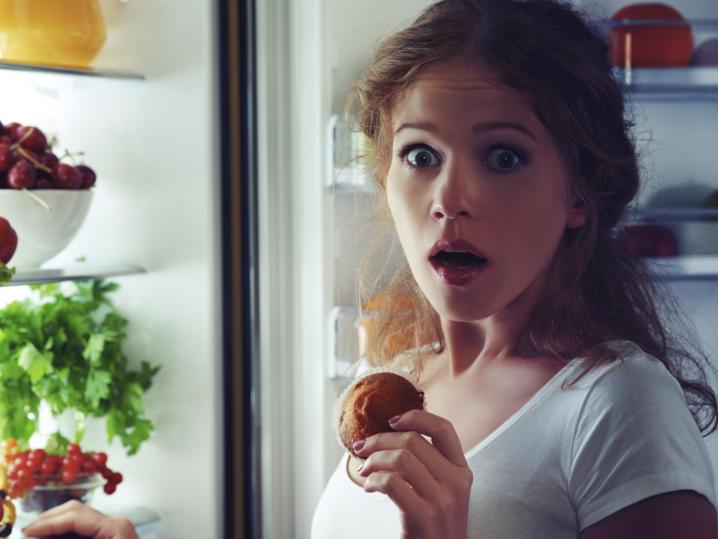 woman eats sweets at night to sneak in a refrigerator