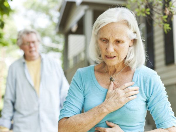 A senior woman experiencing chest pain.  A senior man is in the background.
