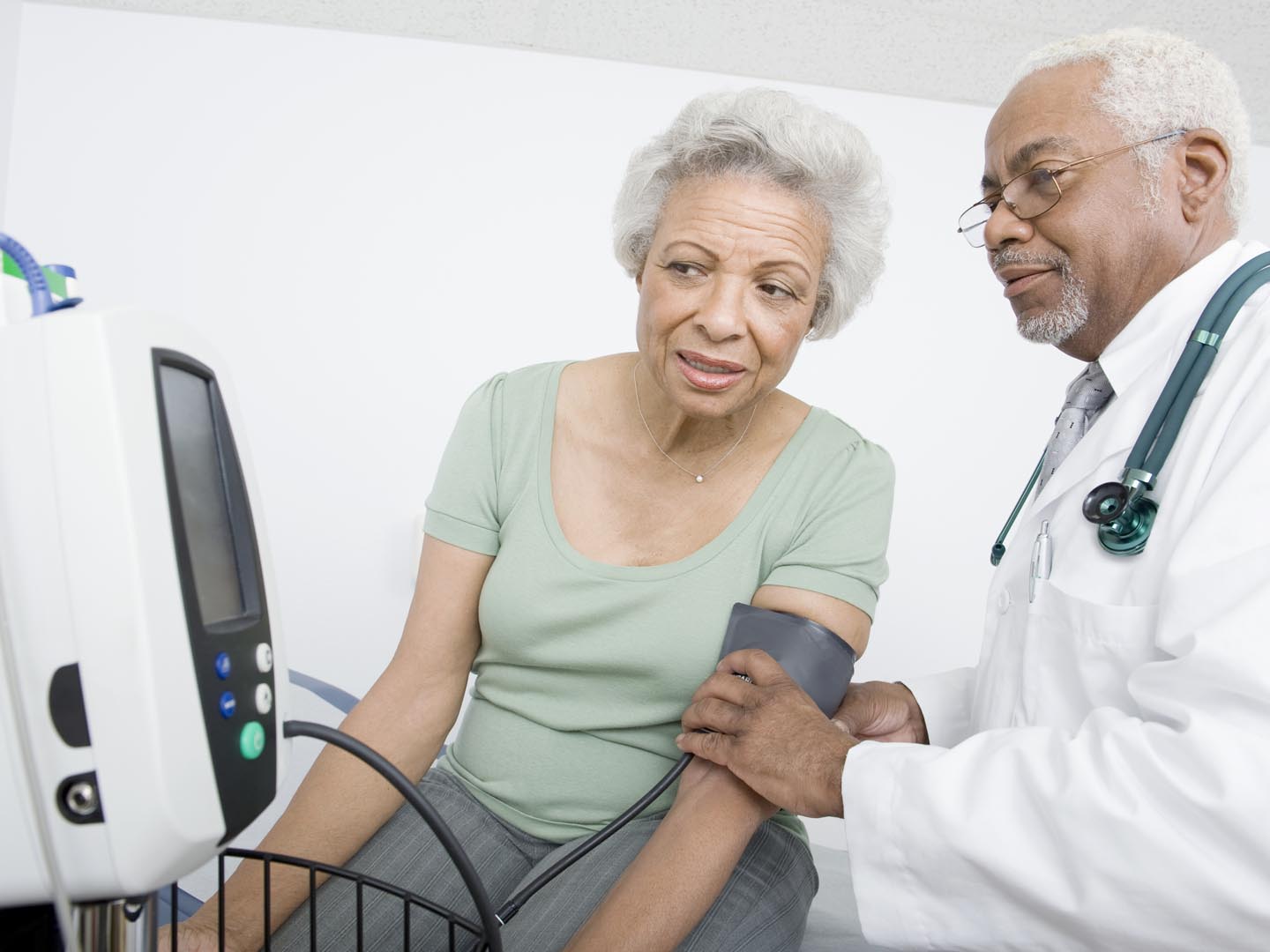 Male doctor checking patient&#039;s blood pressure while looking at machine at clinic