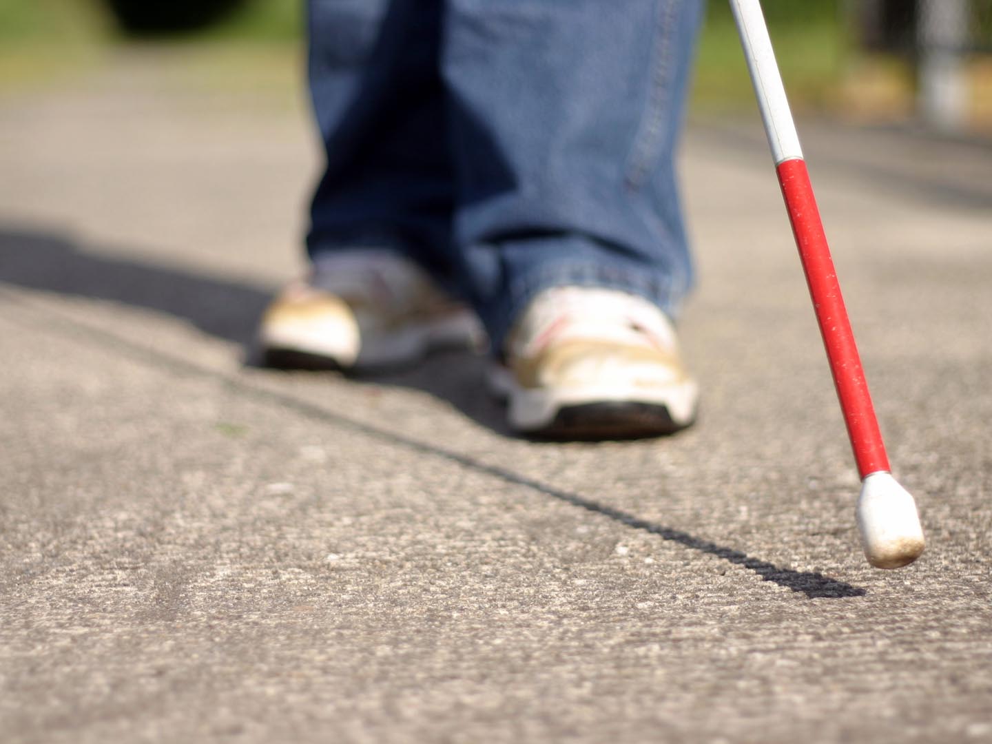 A young cane user feels his way along the sidewalk. Selective focus: Cane in in focus, feet out of focus.