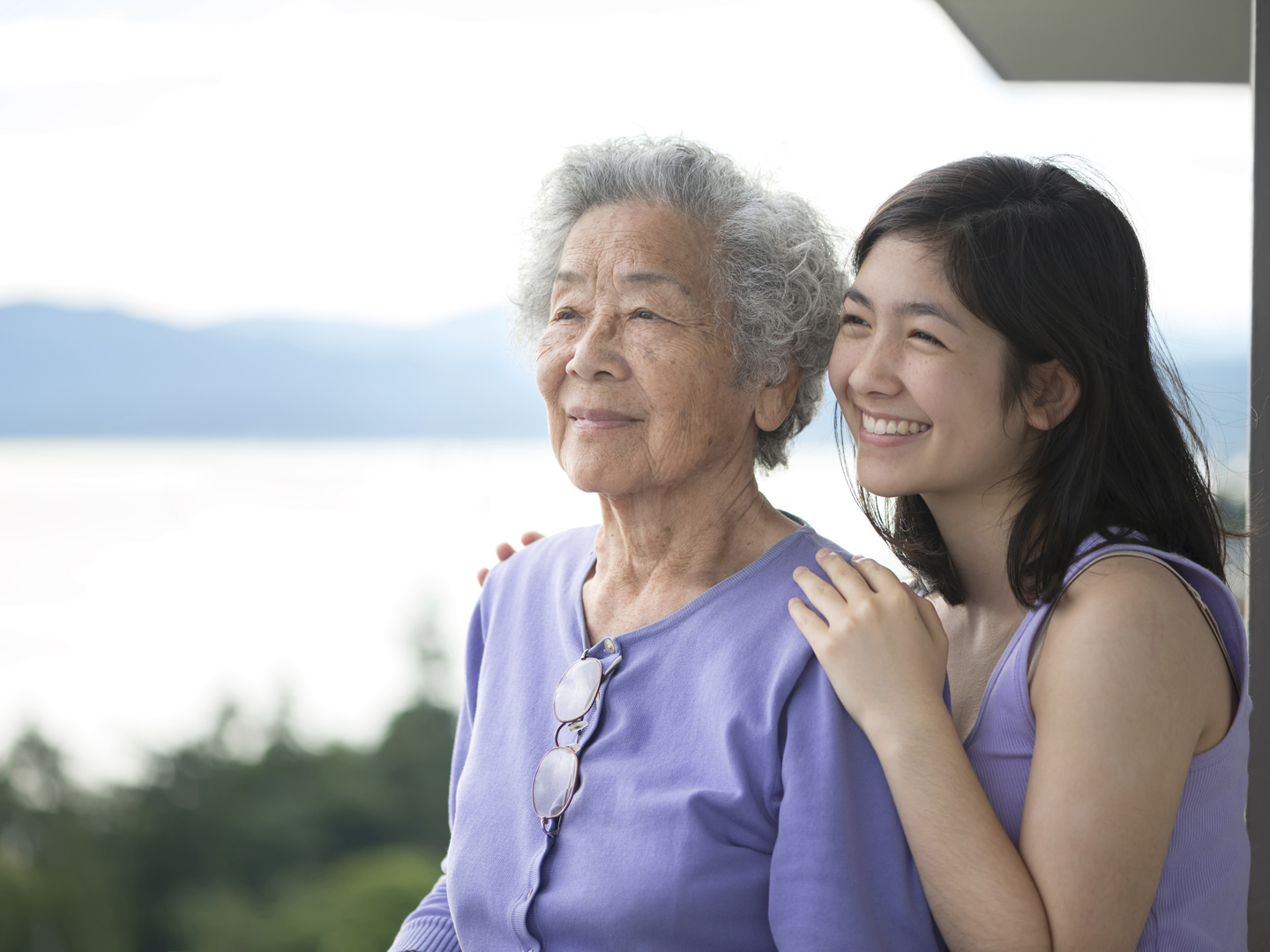 Asian Grandmother and Eurasian granddaughter with park, water and mountains in background.