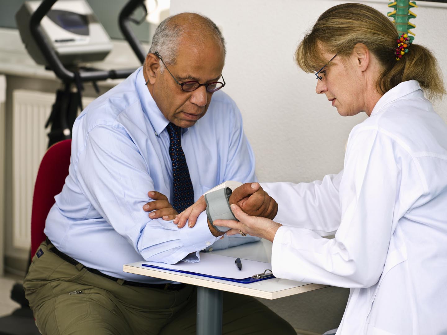 A mature female doctor checks the blood pressure of her male patient using a wrist gauge. Horizontal shot.