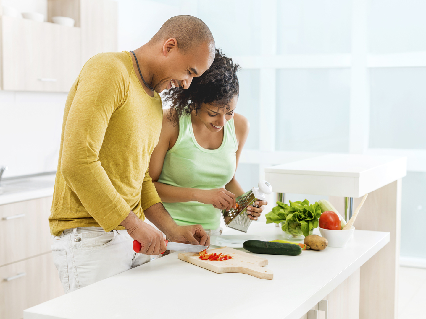 Smiling African American couple preparing food together in the kitchen.