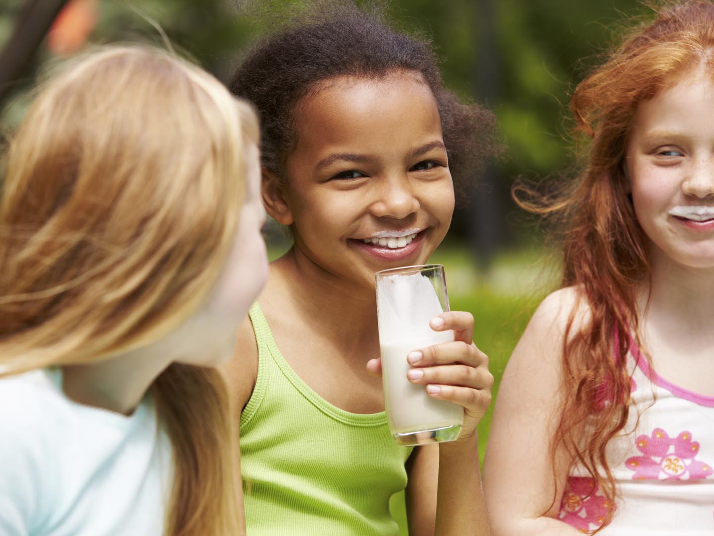 Portrait of cute girl drinking kefir outdoors with her friends near by