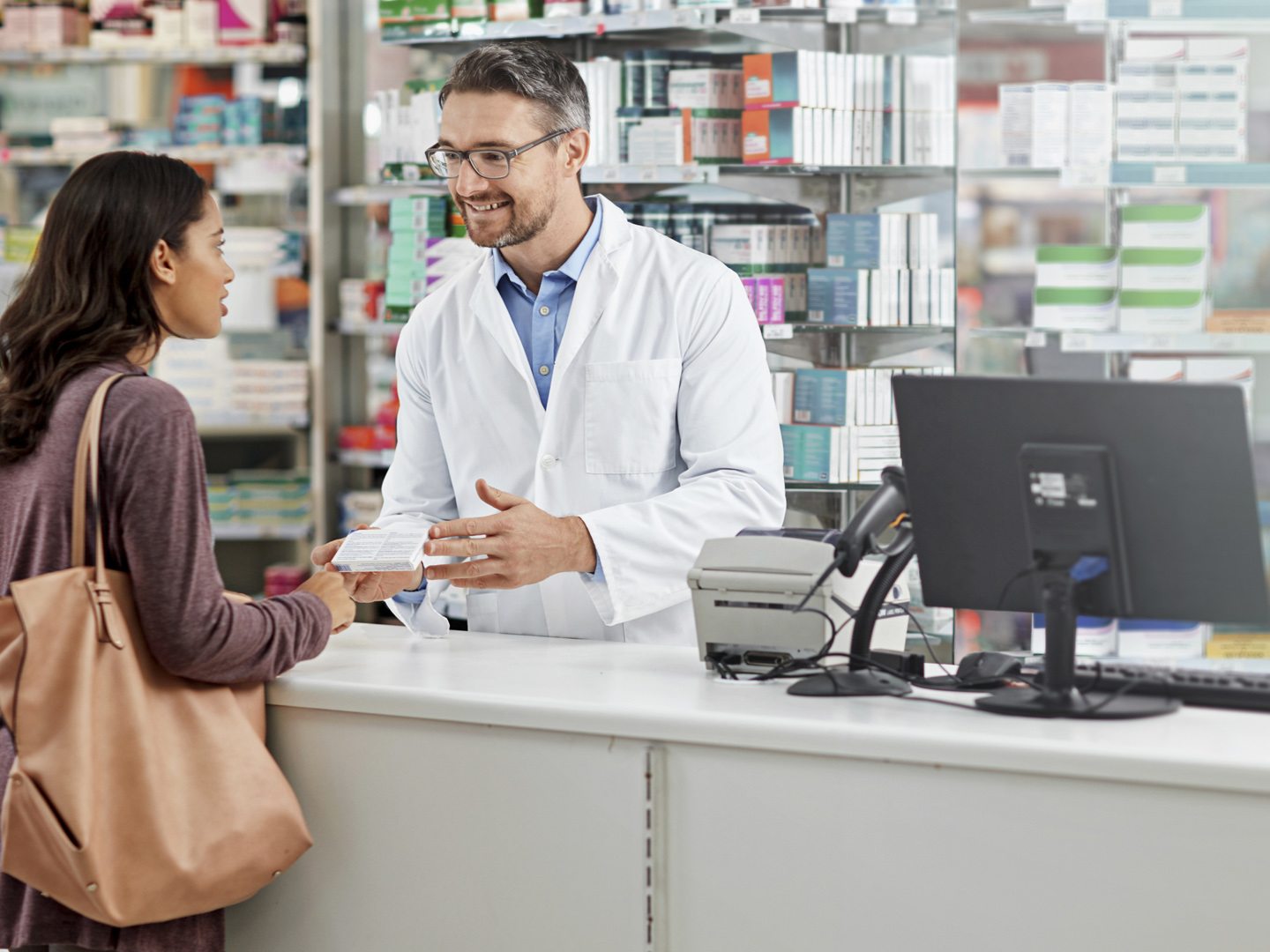 Shot of a male pharmacist assisting a customer at the prescription counter. All products have been altered to be void of copyright infringements