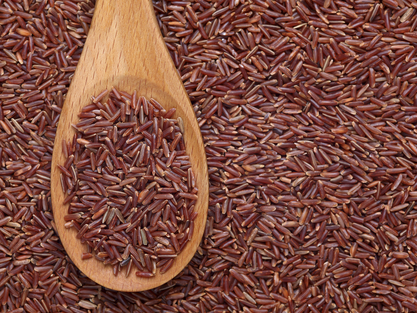 Red rice in a wooden spoon on red rice background.Please see: