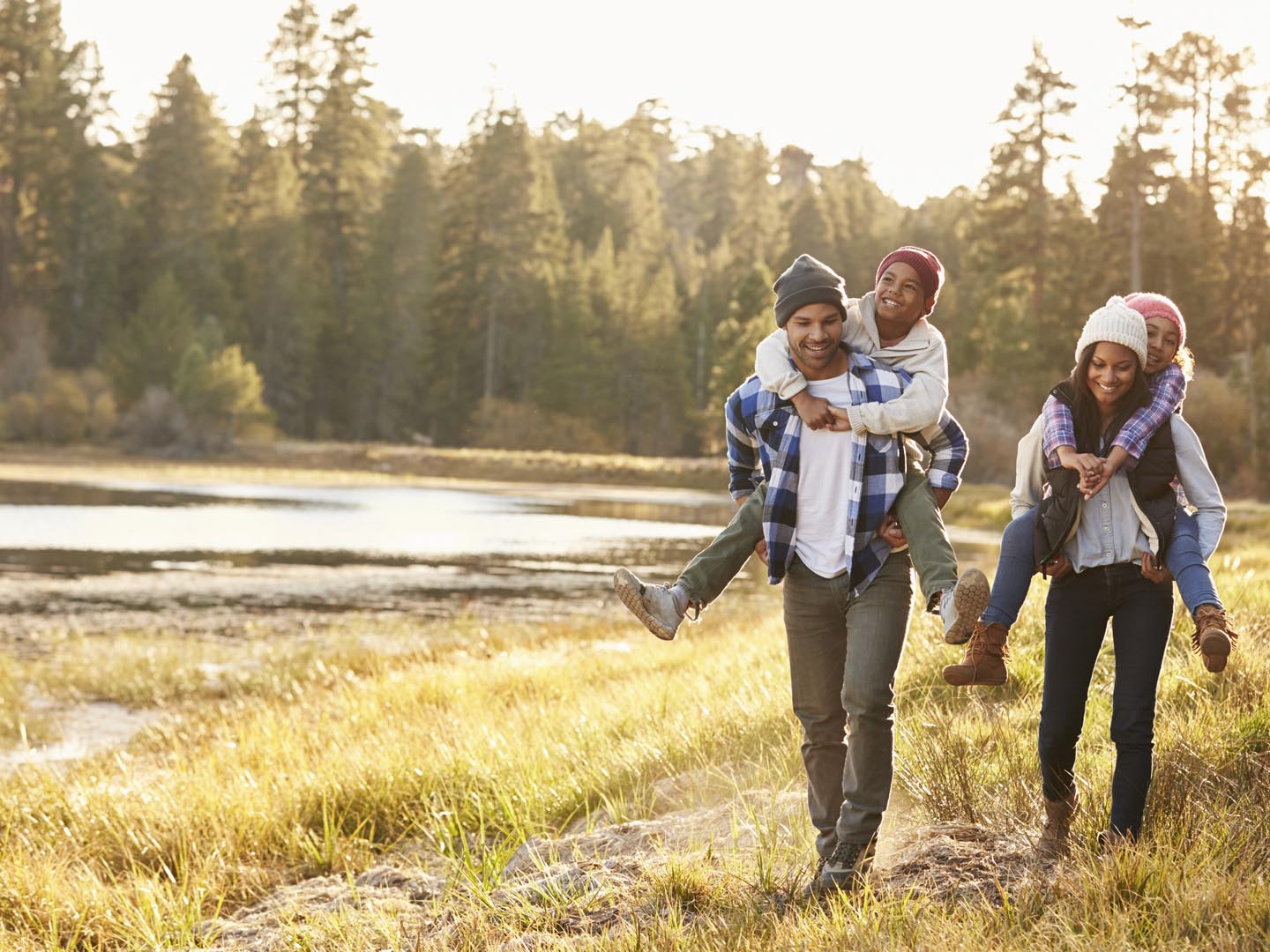 Parents Giving Children Piggyback Ride On Walk By Lake