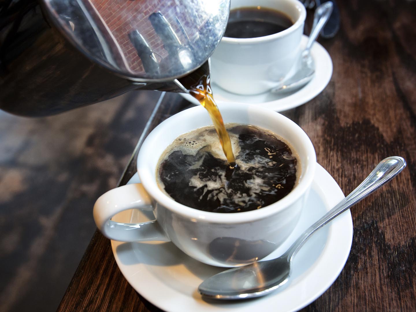 Fresh hot coffee being poured into a cup from a stainless steel french press in a trendy cafe