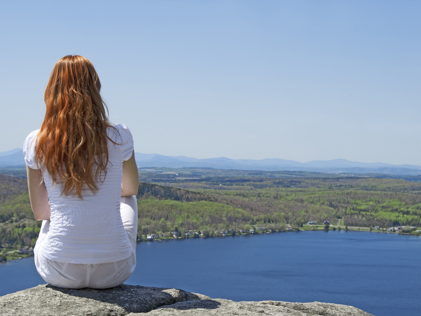 Young woman sitting on top of a mountain, enjoying the view.